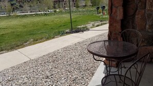 A patio with a table and chairs, a stone wall, and a view of a green field and buildings in the distance.