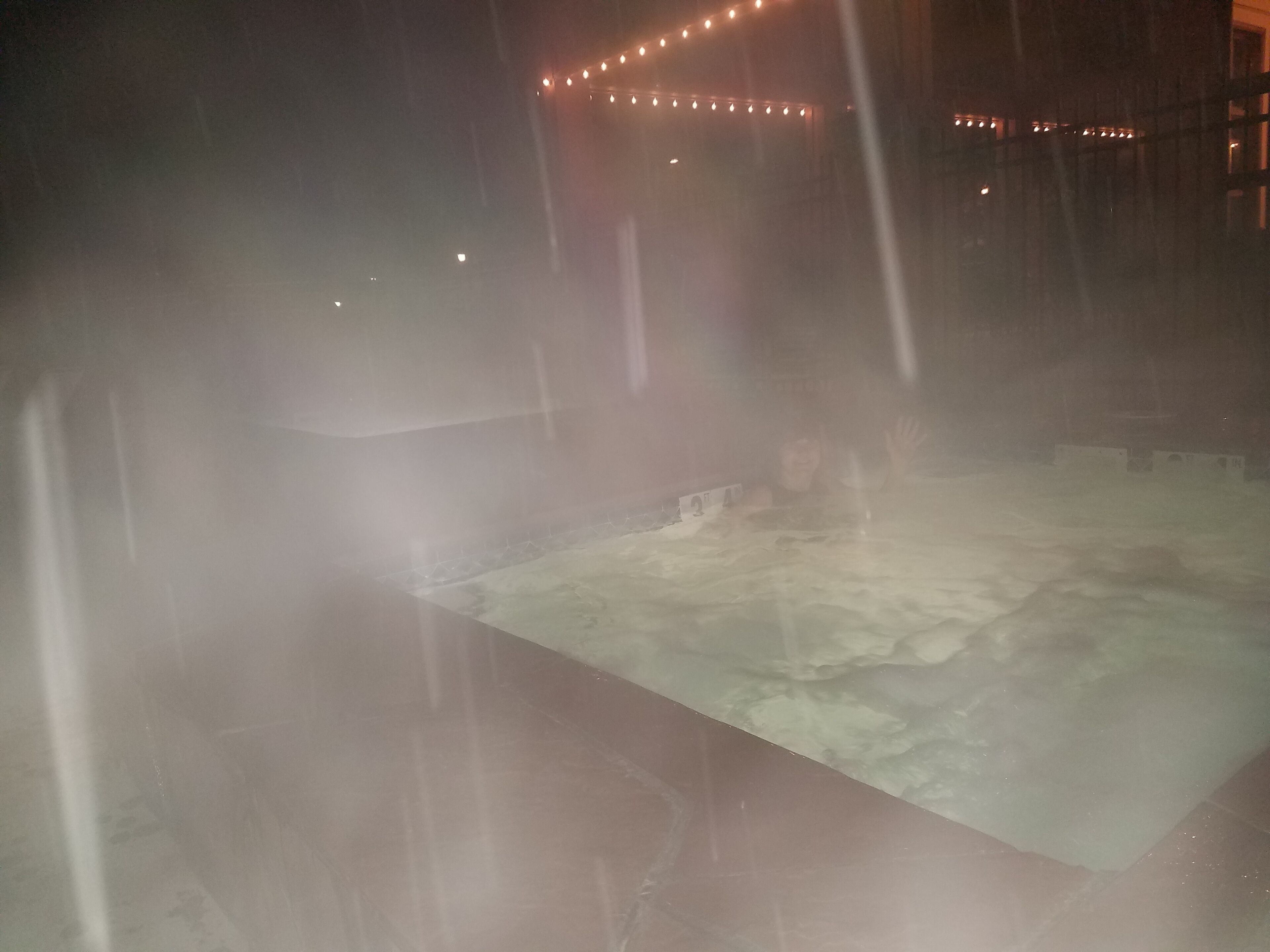 A large indoor pool area with a tiled floor and a person in the water.