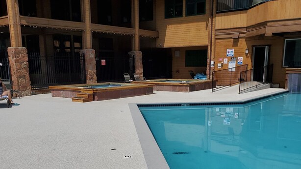 A pool area with a clear blue pool, stone pillars, and a covered seating area with chairs.