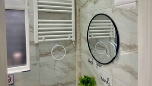Un baño con toallero blanco, espejo con marco negro y un letrero que dice "Lávate las manos".