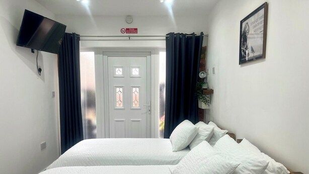 Habitación de hotel con dos camas, un televisor de pantalla plana montado en la pared, una puerta con el cartel de detector de humo y un cuadro enmarcado.