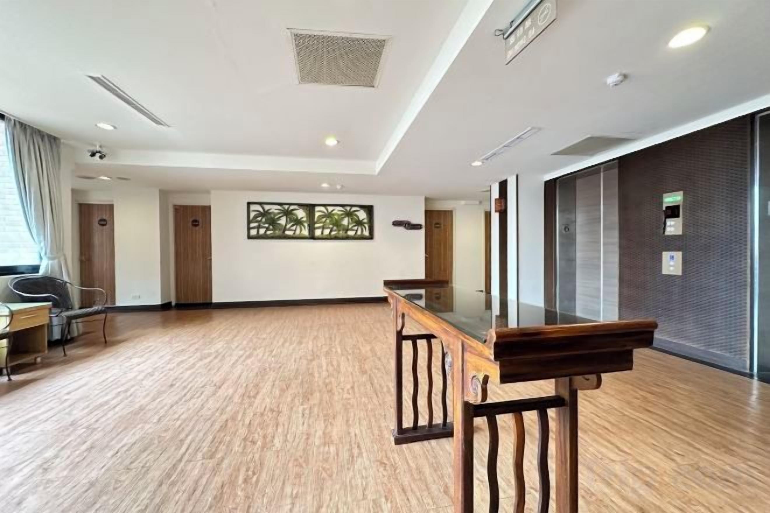 A hotel room with a wooden floor, a reception desk, and a large window with a view.