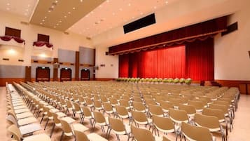 Un salón amplio con filas de sillas y un escenario con cortina roja.