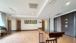 Una habitación amplia con suelo de madera, una mesa con superficie de vidrio y un rincón de descanso con sillas.