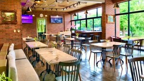 Un restaurante con paredes de ladrillo, ventanas amplias y diferentes opciones de asientos, incluyendo mesas y bancos.