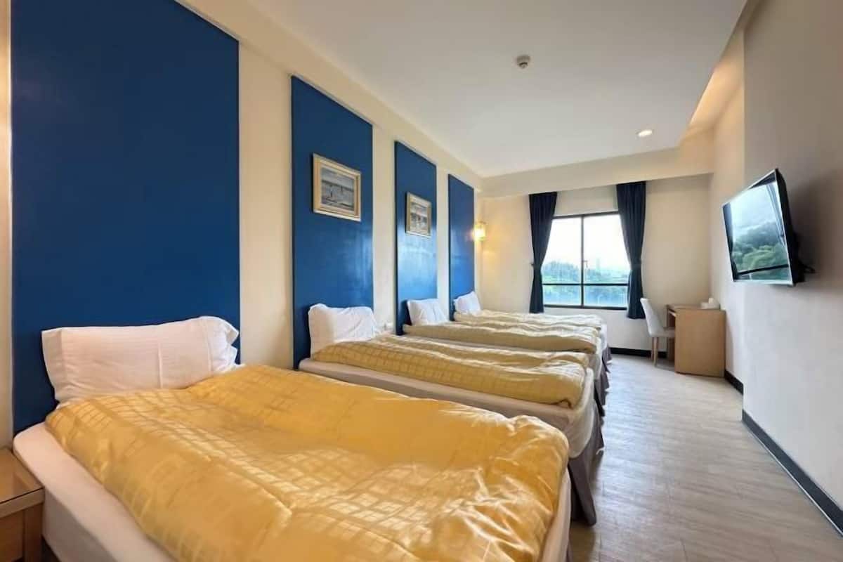Une chambre d’hôtel avec trois lits, une télévision et un bureau.