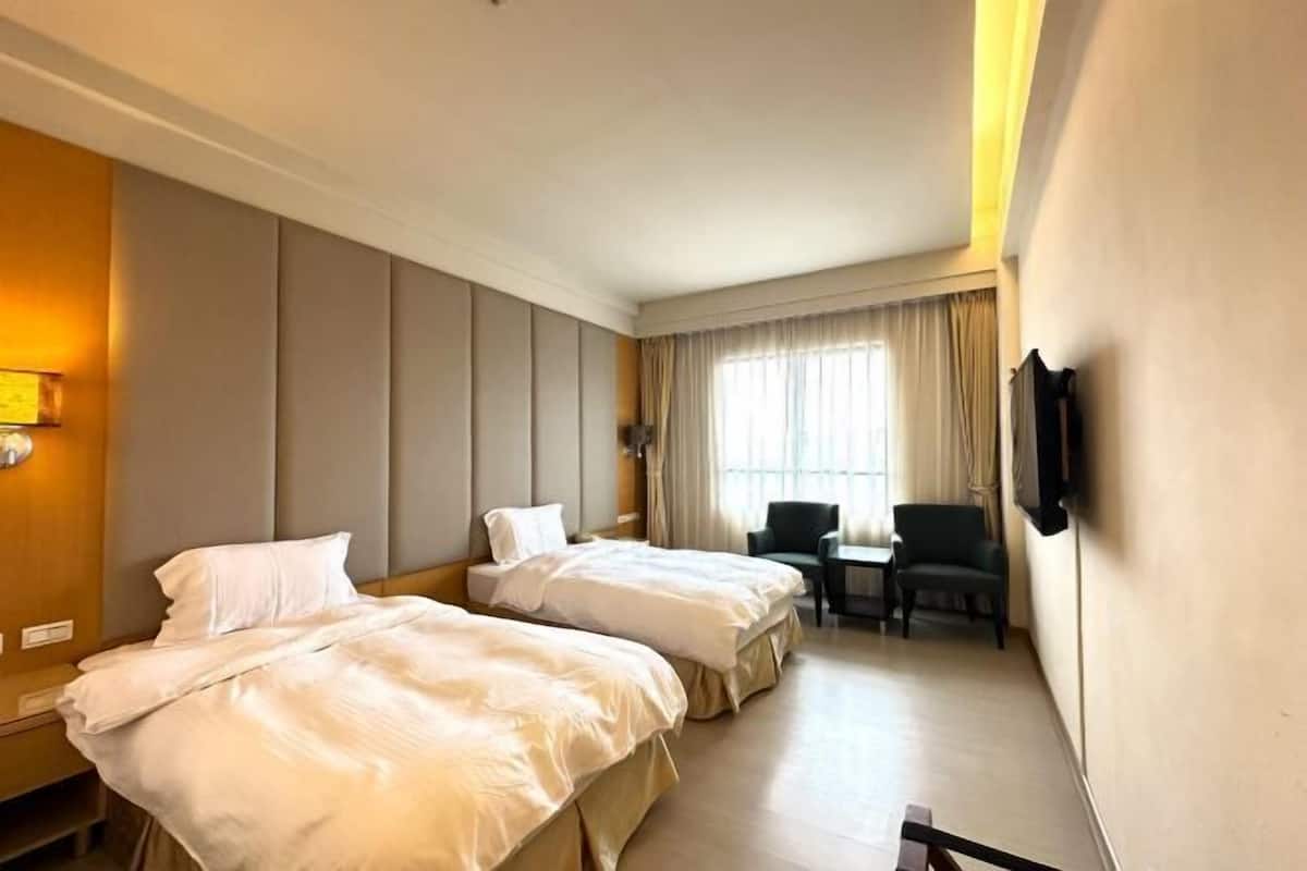 Une chambre d’hôtel avec deux lits, un bureau, des chaises, une télévision et une fenêtre avec des rideaux.