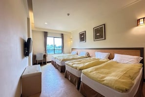 Ein Hotelzimmer mit drei Betten, einem Schreibtisch, einem Sessel und einem Fernseher.