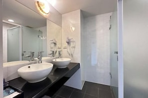 Ein modernes Badezimmer mit zwei großen weißen Waschbecken, einem Spiegel und einer Duschkabine aus Glas.