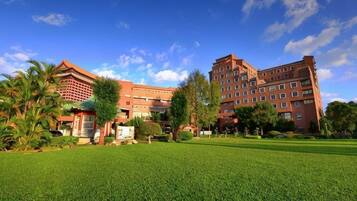 Um hotel com um extenso gramado em primeiro plano, um edifício vermelho com vários andares e um céu azul límpido.