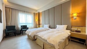 Habitación de hotel con dos camas, un escritorio, una silla y un ventanal con cortinas.