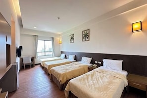 Ein Hotelzimmer mit drei Betten, einem Schreibtisch und einem Sessel.