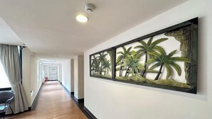 Un pasillo con suelo de madera, una obra de arte en la pared con palmeras y una silla junto a la ventana.