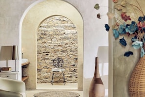 A room with a stone wall, a white chair, a round table, and a vase. - Villa Paz - La Villa Group (Camocim)