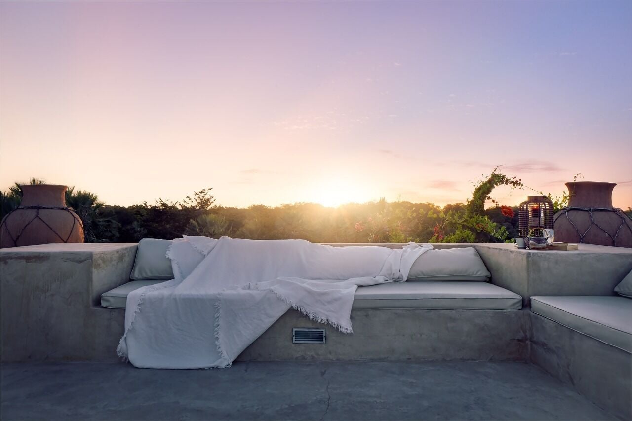 Un espacio de estar en la azotea con una manta blanca, dos jarrones grandes y vistas al atardecer.