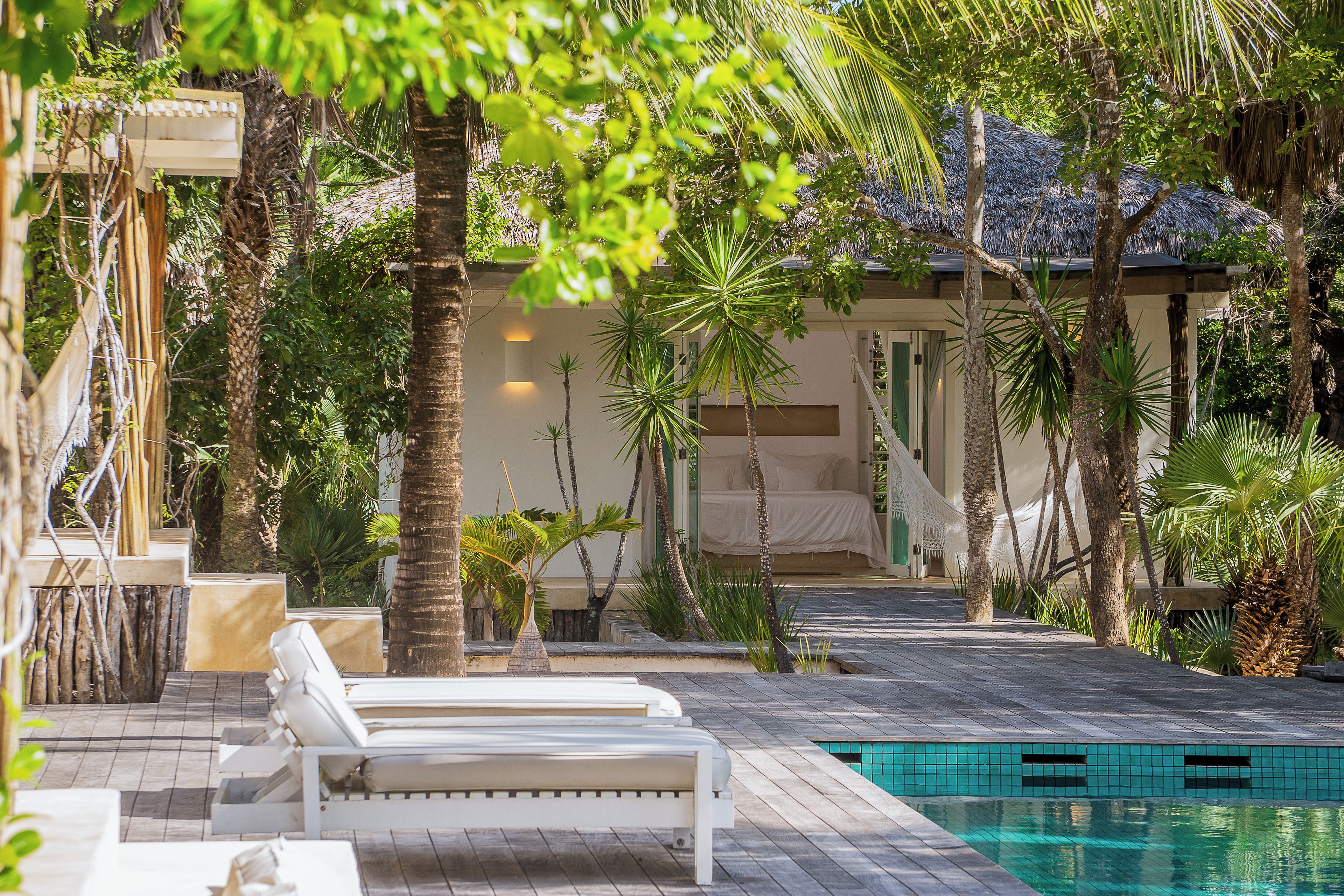 Un área de piscina con sillones de descanso, una piscina pequeña y vegetación tropical.