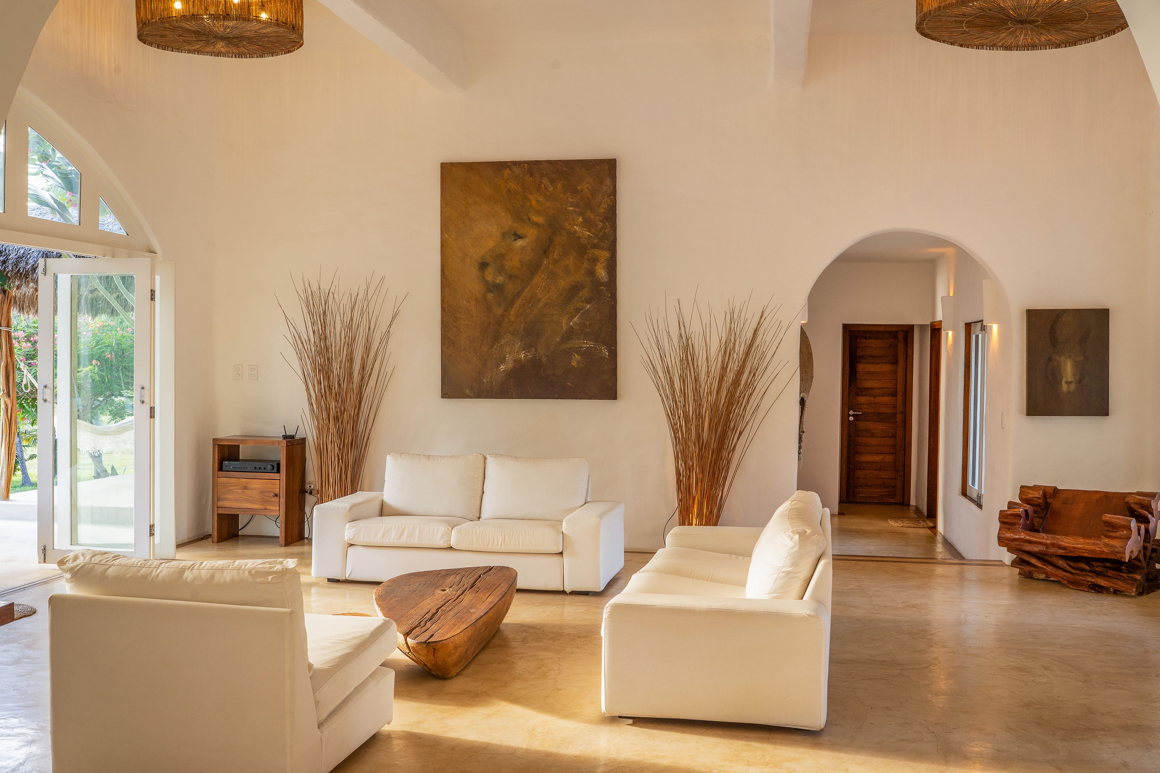 A spacious living room with a white sofa set, a wooden coffee table, and a large abstract painting on the wall.