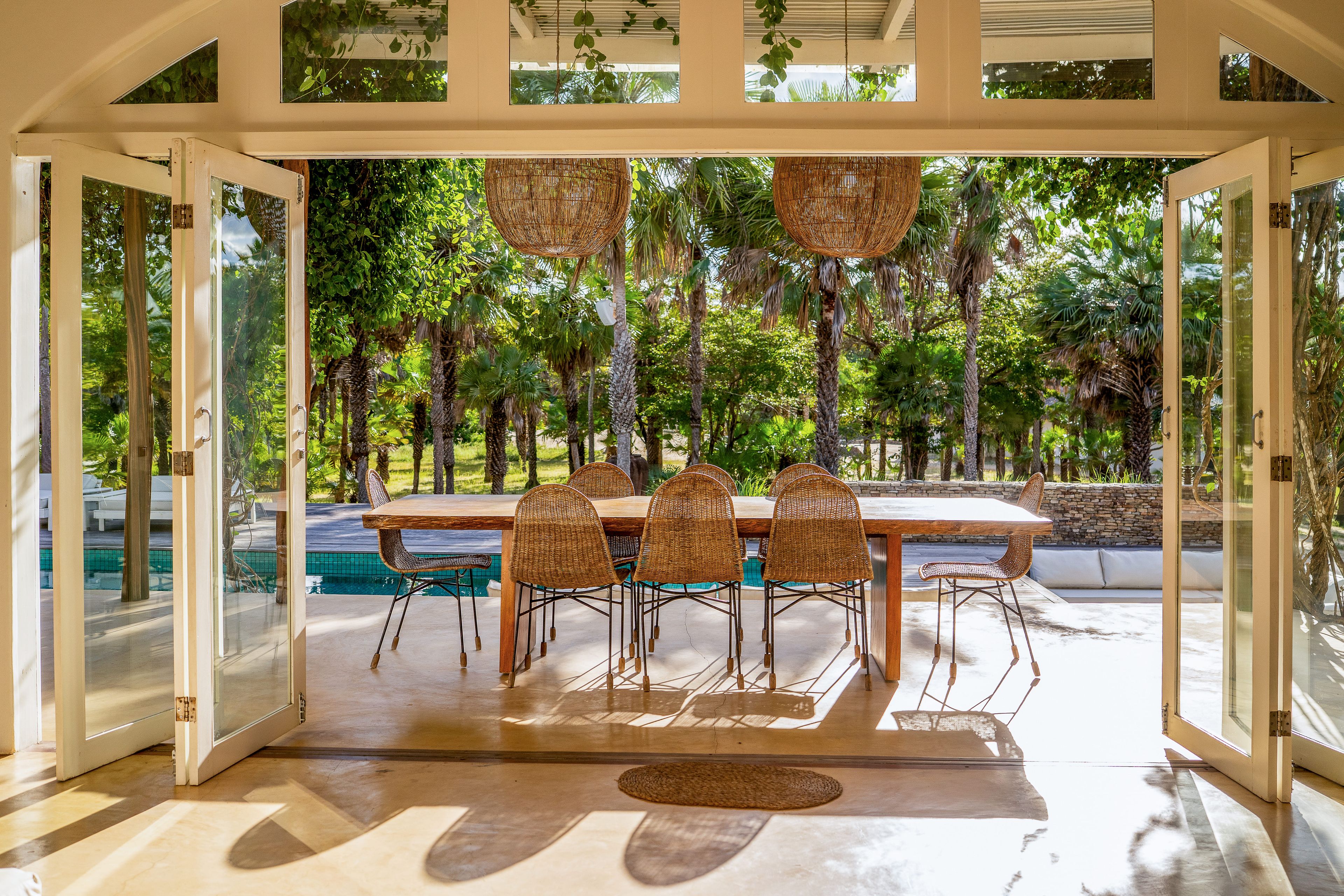 Un comedor de planta libre con vista a la piscina, que incluye una mesa de madera y sillas de mimbre.