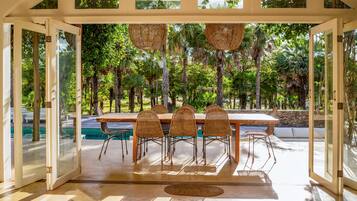 Un comedor de planta libre con vista a la piscina, que incluye una mesa de madera y sillas de mimbre.