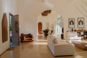 A spacious living area with a white sofa, wooden coffee table, and a dining table with chairs. An arched doorway leads to another room. - Villa Paz - La Villa Group (Camocim)