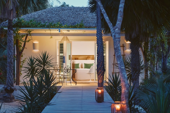 Une villa moderne dotée d’une terrasse en bois, d’une chambre avec un lit et une table de chevet, et d’un coin repas avec des chaises et une table.
