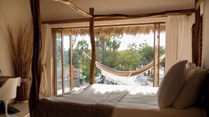 Un dormitorio con cama, hamaca y vistas a un jardín tropical.