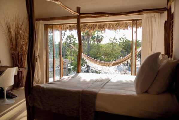A bedroom with a bed, a hammock, and a view of a tropical garden. - Villa Paz - La Villa Group (Camocim)