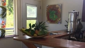 Una cocina con encimera de madera, un cuenco de fruta, una cafetera y un cuadro en la pared.