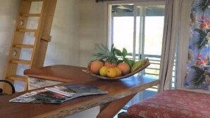 Una habitación con cama tipo altillo, una escalera de madera, una mesita con fruteros y un ventanal con cortinas.