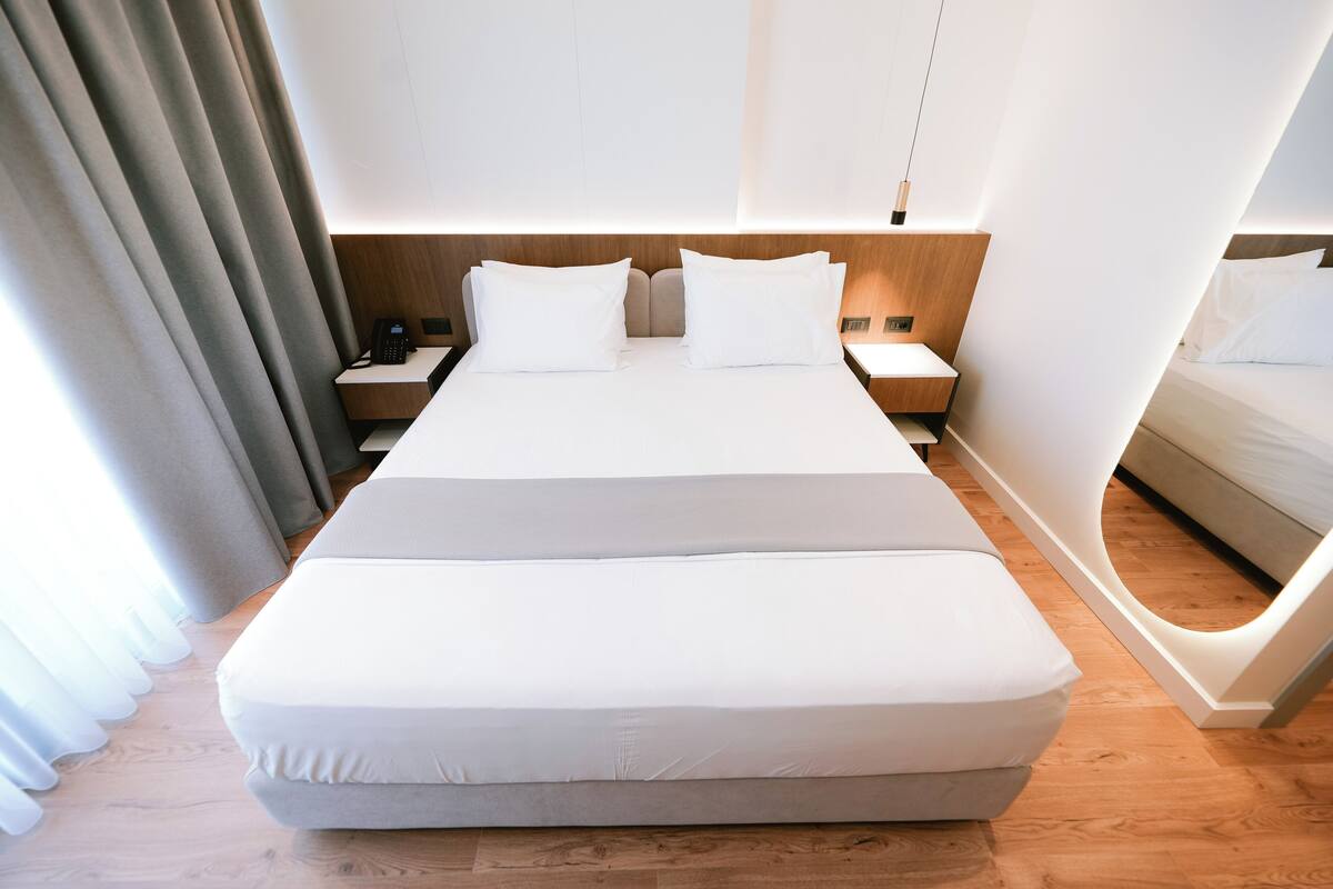 Une chambre d’hôtel moderne avec un grand lit, une tête de lit en bois, des tables de chevet et une palette de couleurs neutres.