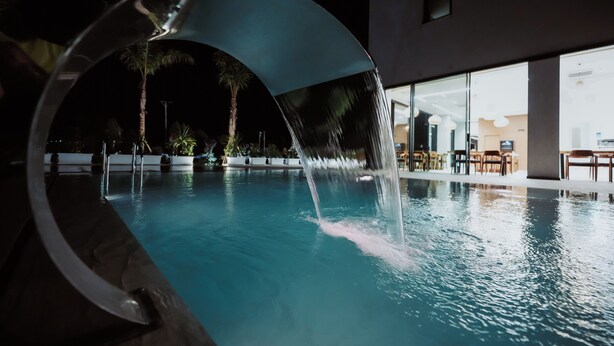 A pool with a water feature, surrounded by a modern building with large windows. - Euro Hotel (Ksamil)