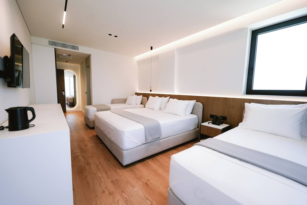 Une chambre d’hôtel moderne équipée d’un grand lit, d’un lit plus petit, d’un bureau et d’une télévision.