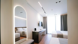 A modern hotel room with a bed, a bench, a desk, a flat-screen TV, and a large window with curtains. - Euro Hotel (Ksamil)