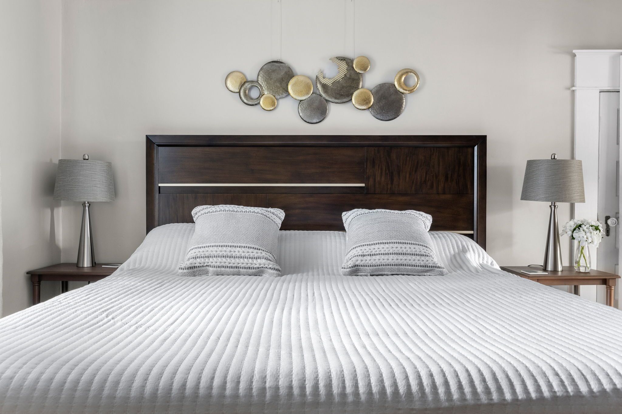 Een netjes opgemaakt bed met een witte, geribbelde deken, twee bijpassende kussens en een donker houten hoofdbord.