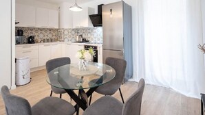 Una cocina moderna con armarios blancos, un refrigerador de acero inoxidable y una mesa de comedor de vidrio con cuatro sillas grises.
