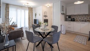Una sala moderna con una mesa redonda de vidrio y cuatro sillas grises, un sofá gris y una cafetera en la zona de la cocina.
