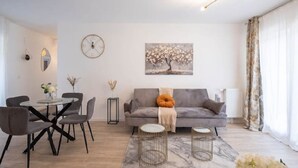 Una sala de estar moderna con un sofá gris, una mesa de comedor redonda con sillas, una mesa de centro y un cuadro en la pared.