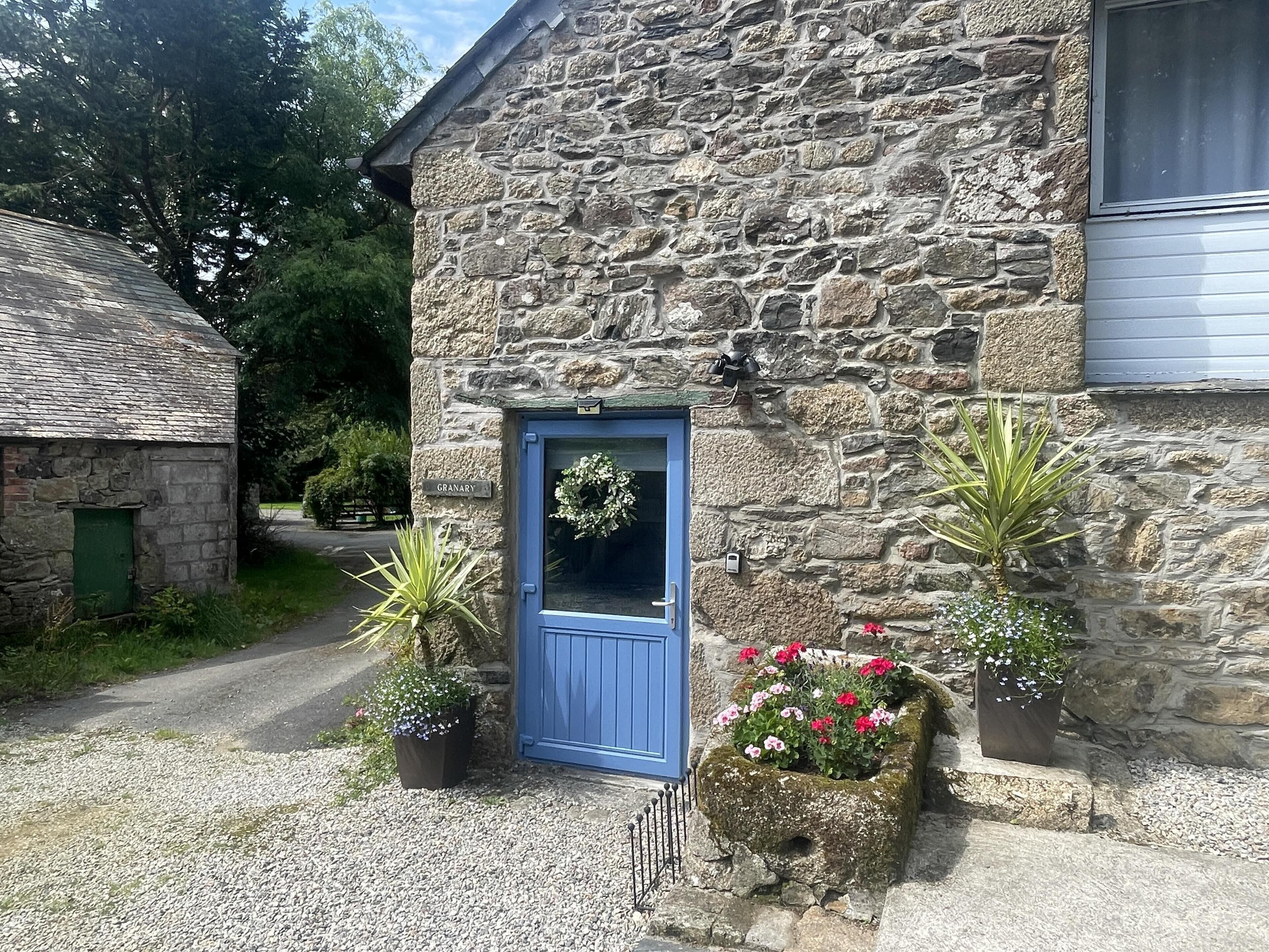 Ein Steinhaus mit blauer Tür, ein kleiner Garten mit Topfpflanzen und einem Kiesweg.
