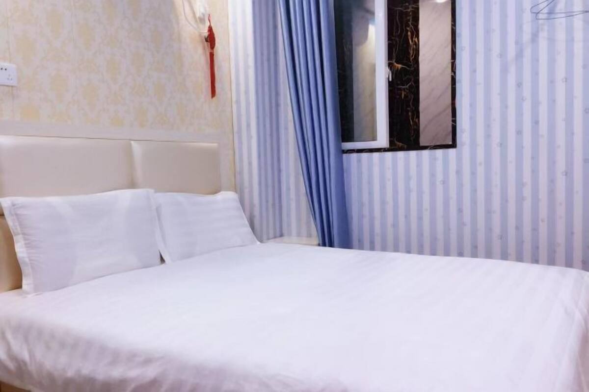 Una cama con ropa de cama blanca en una habitación con papel tapiz a rayas y una ventana con cortinas azules.