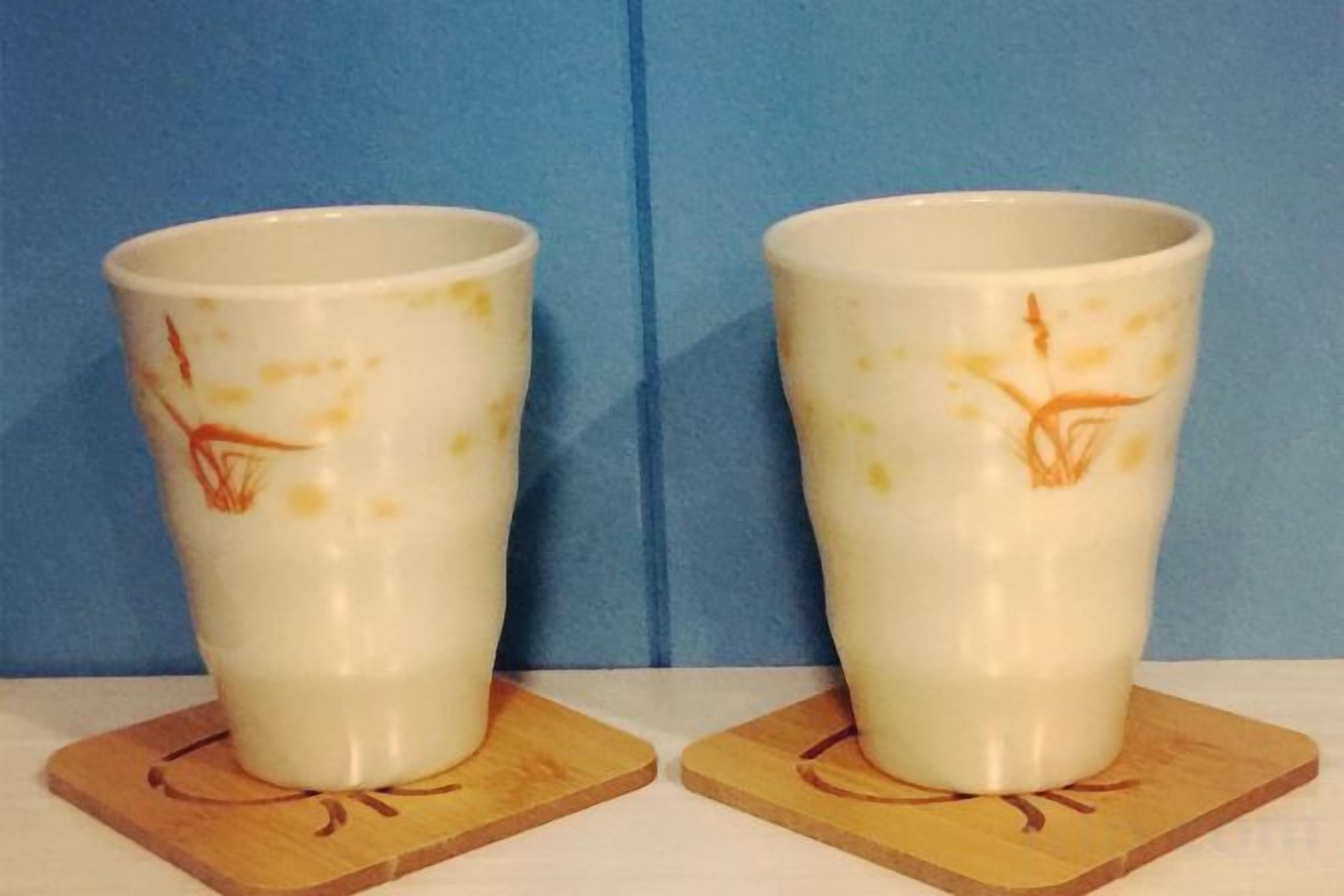 Two white ceramic cups with orange designs on a wooden coaster against a blue background.