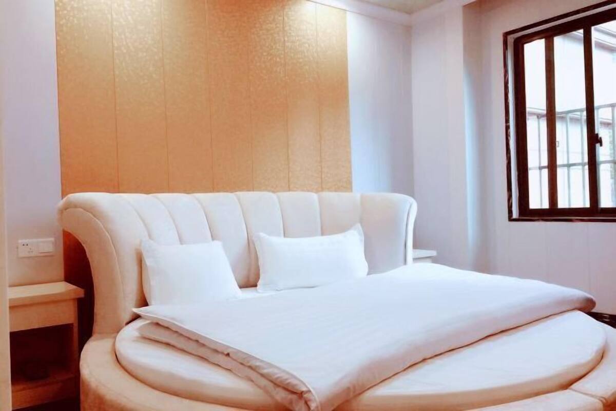 Una cama con cabecera curva, una mesita de noche y una ventana con rejas.