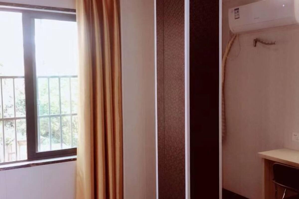 Una habitación con ventana, aire acondicionado y un pequeño escritorio.