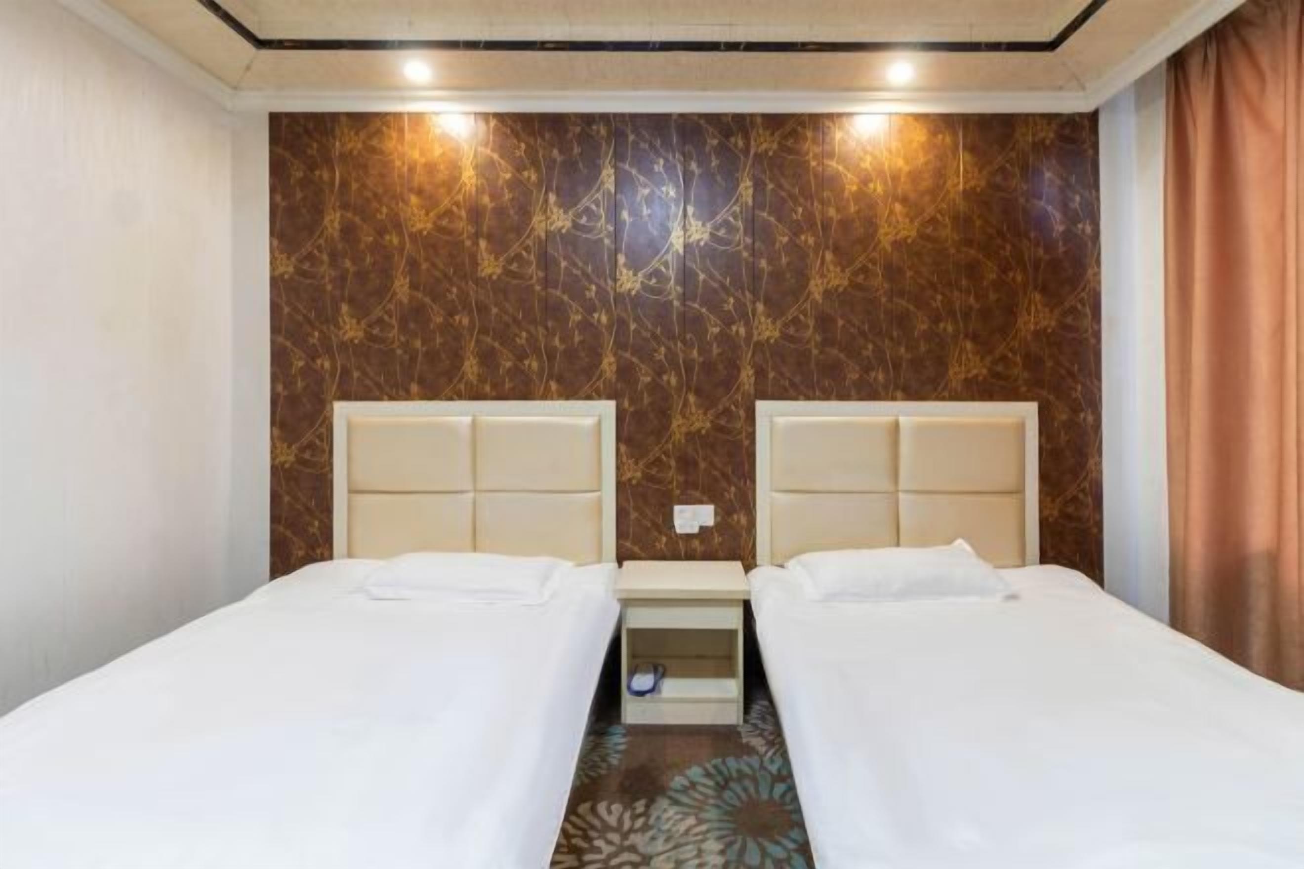 A hotel room with two beds, a marble-patterned wall, and a small bedside table.