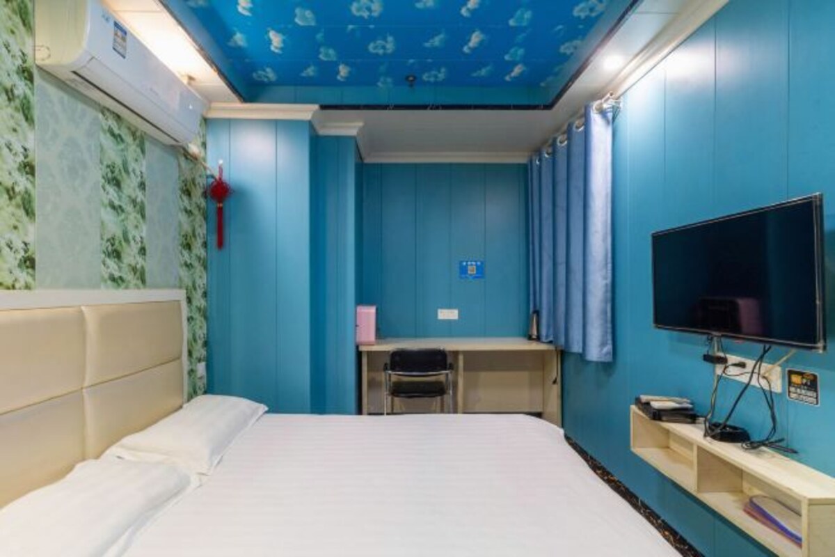 Ein Zimmer mit einem Bett, einem Schreibtisch, einem Stuhl, einem Fernseher und einer blauen Wand.