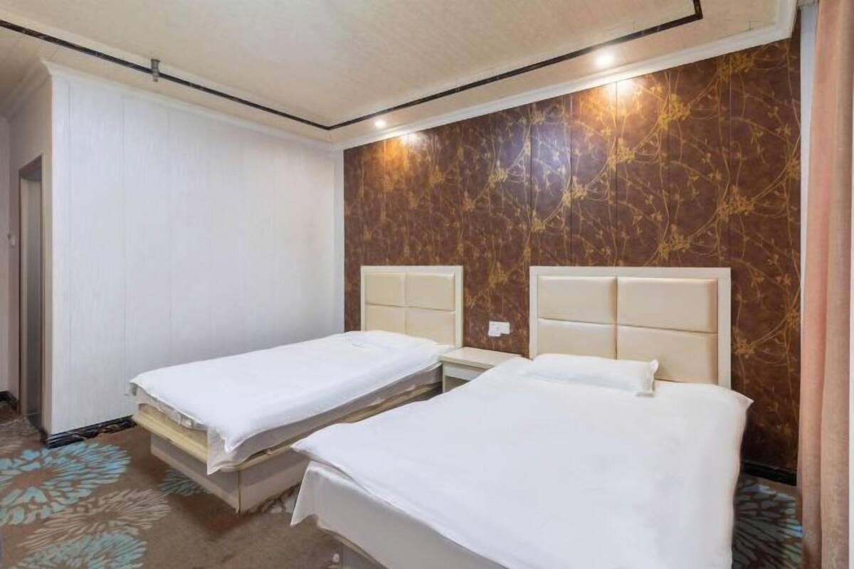 Una habitación de hotel con dos camas individuales, un muro con diseño de mármol y una puerta a la izquierda.