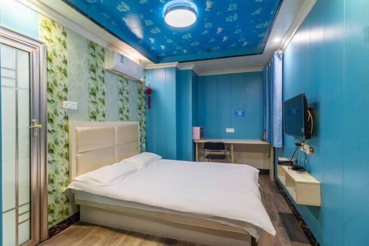 Una habitación de hotel con cama, escritorio, televisor y una lámpara en el techo.