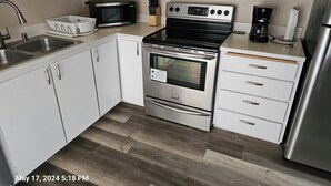 A modern kitchen with white cabinets, a stainless steel stove, a microwave, and a refrigerator. - Marine View Townhouse (Everett)