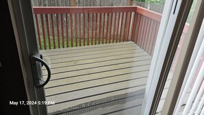 A wooden deck with a red railing, a door, and a view of a backyard with a wooden fence and trees. - Marine View Townhouse (Everett)