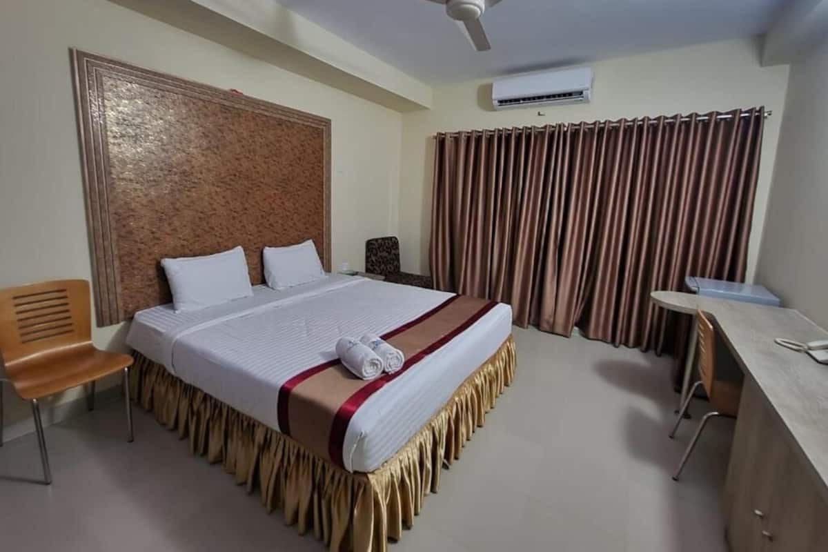 A hotel room with a bed, a desk, a chair, a ceiling fan, and curtains.