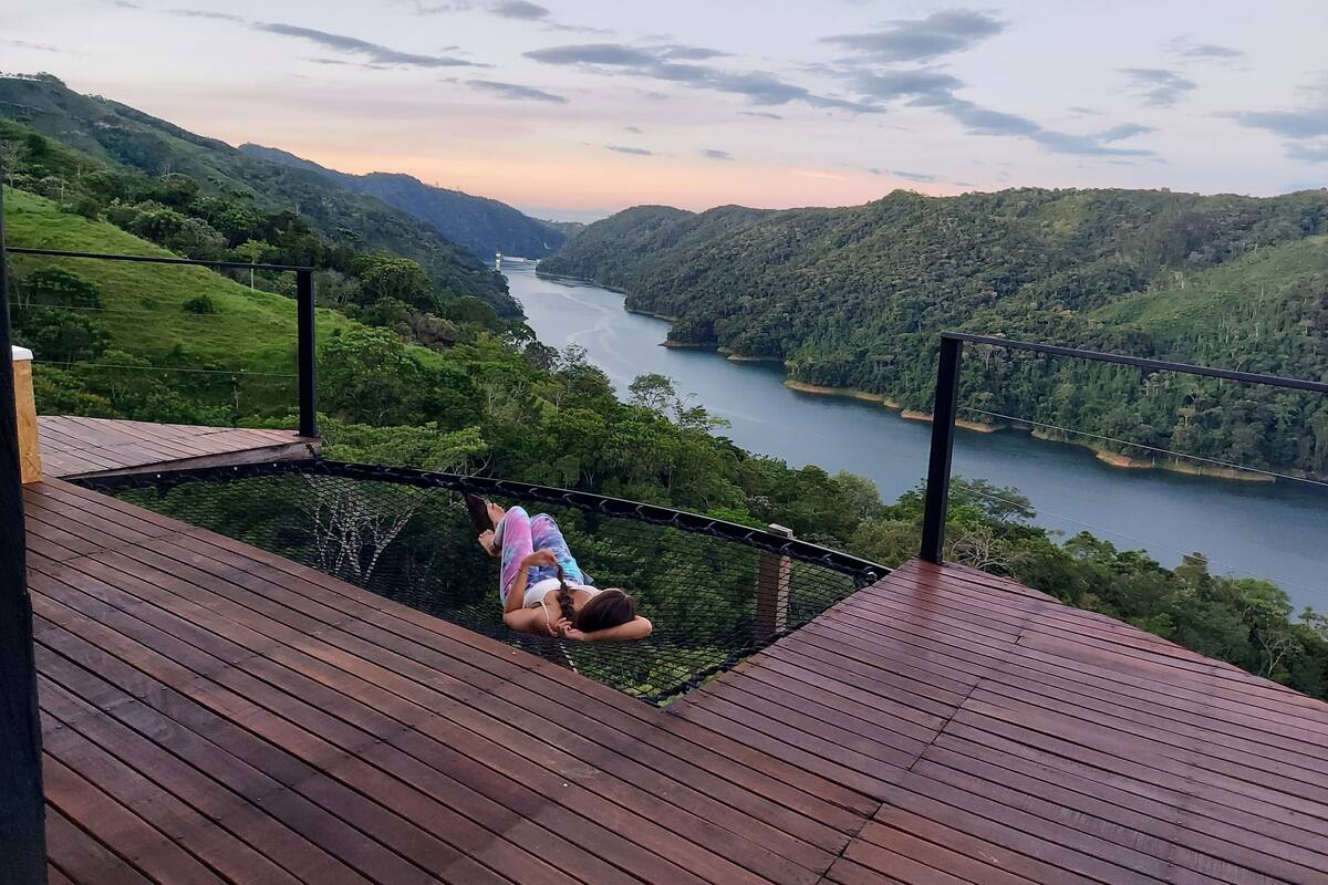A person on a wooden platform overlooking a river and hills.